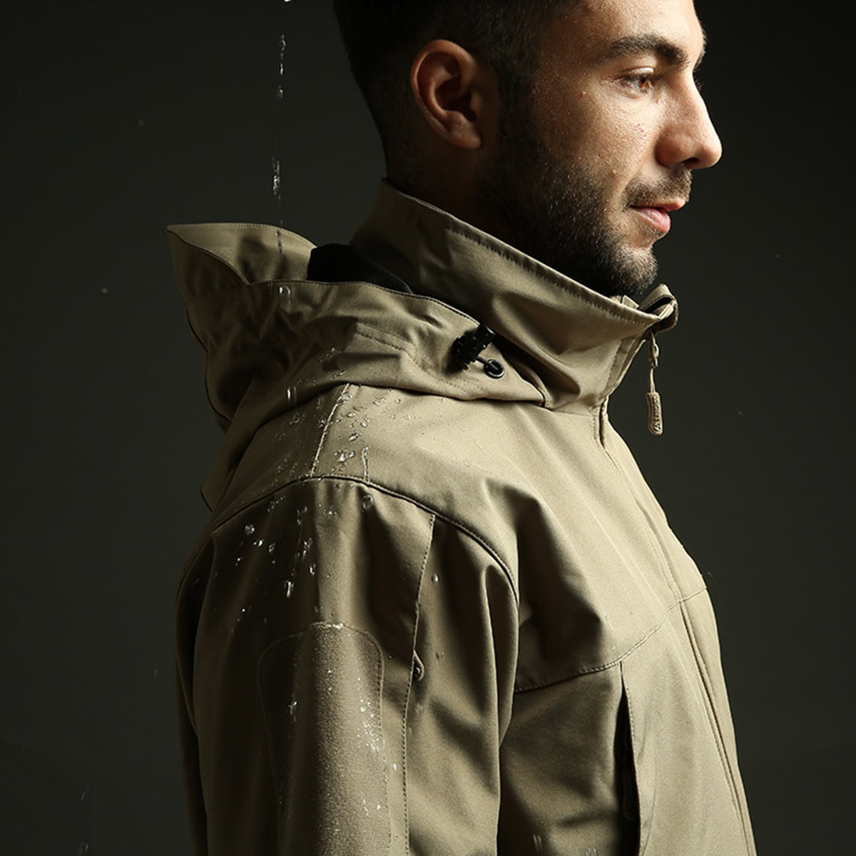 A man wearing the Onken waterproof tactical jacket in the rain, demonstrating the water-beading performance of the DWR-coated softshell fabric.