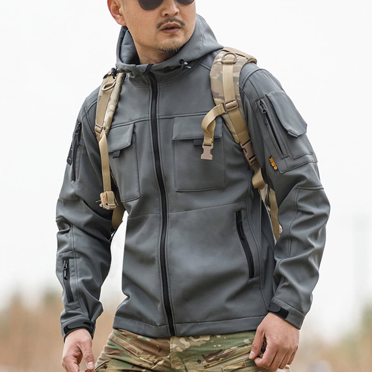 Operator wearing the grey Onken Beetle fleece lined tactical jacket, showing the arm pocket detail and seamless integration with tactical gloves and a backpack.