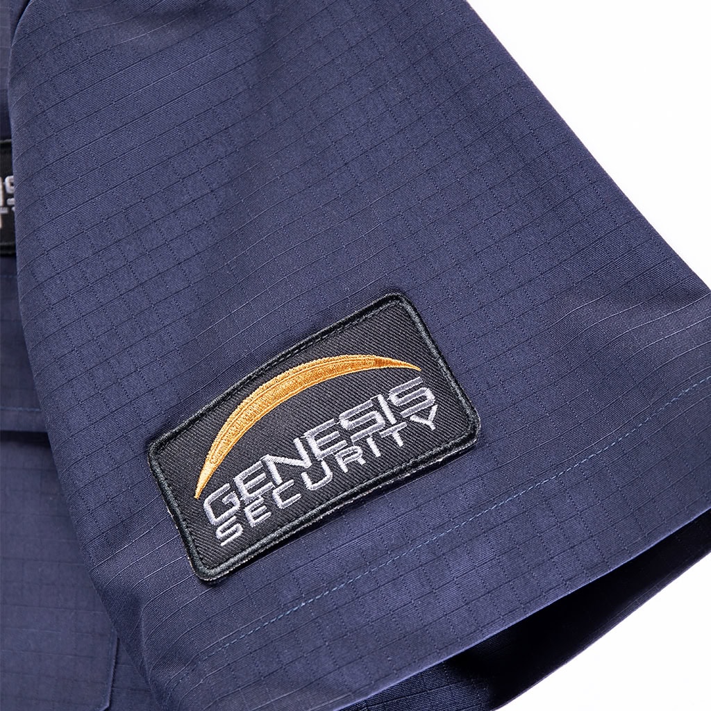 Close-up of a custom "Genesis Security" arm badge attached to the velcro panel on the sleeve of the navy blue ripstop security shirt.