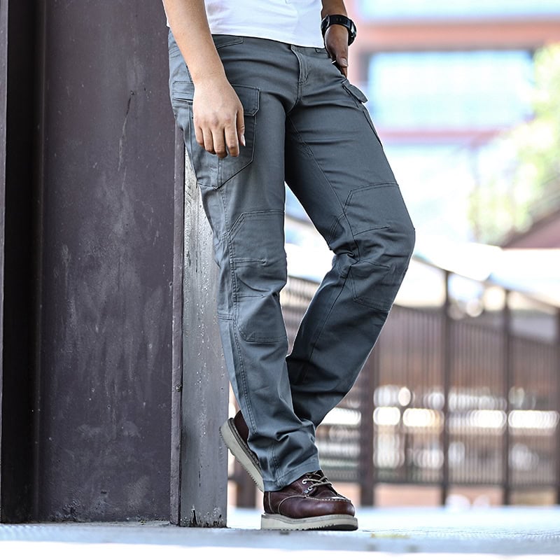 A man in a relaxed stance wearing the custom ripstop IX7 tactical pants in Grey Green, showing articulated knees.