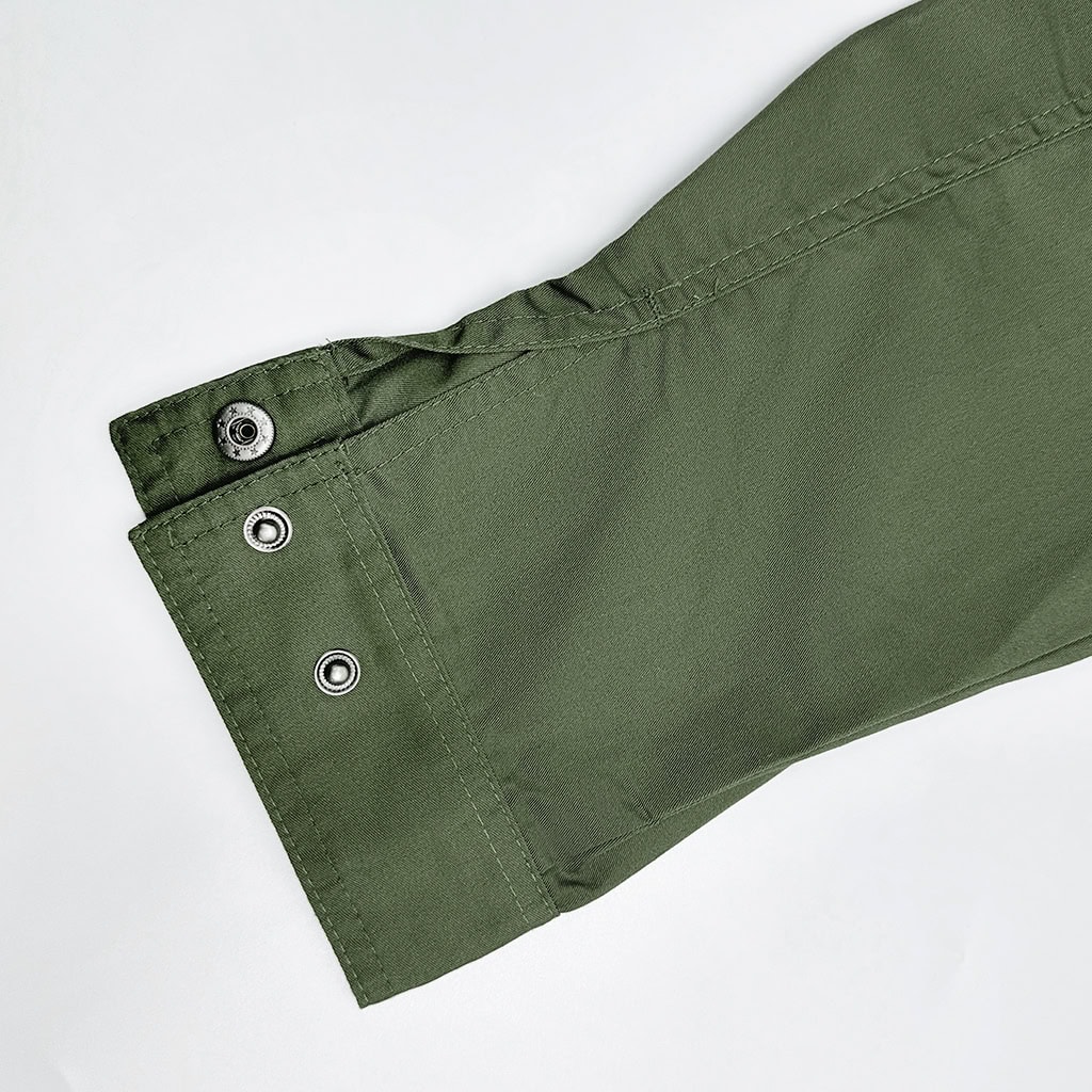 Detail of the adjustable snap-button cuff on the sleeve of the custom olive green tactical shirt.