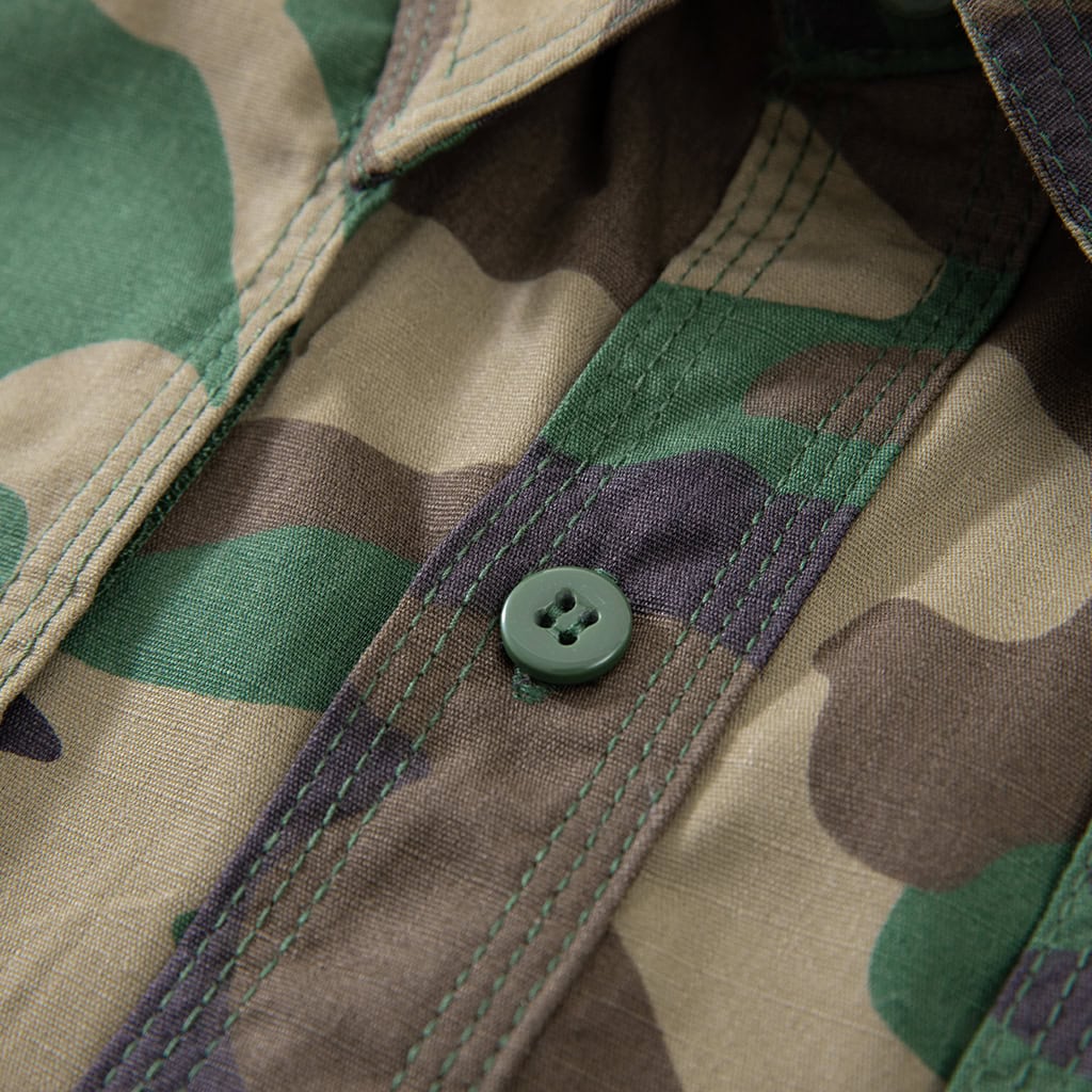 Close-up of a durable button on the front placket of the custom woodland camo short sleeve BDU shirt.